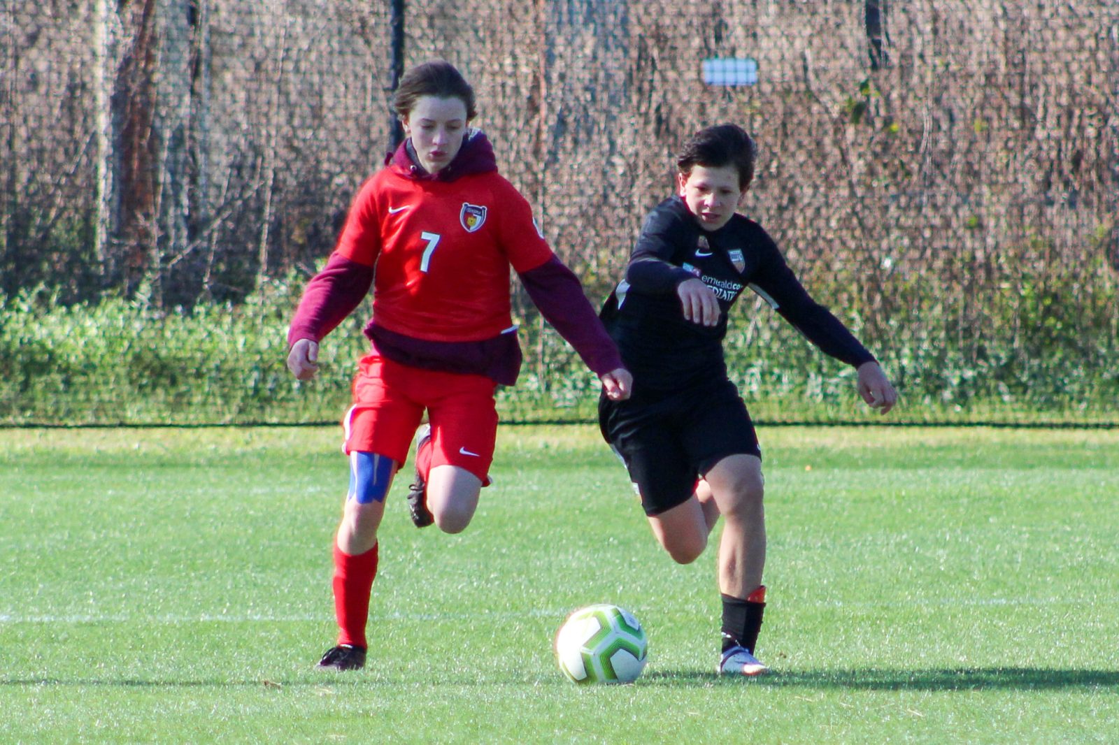Two soccer players in uniforms running for the ball